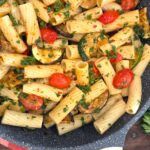 A wide overhead shot of a fresh skillet of zucchini and cherry tomato pasta served hot on a rustic outdoor dining table.