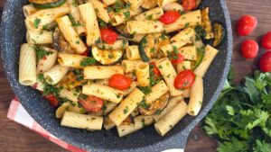 A wide overhead shot of a fresh skillet of zucchini and cherry tomato pasta served hot on a rustic outdoor dining table.
