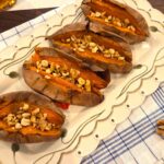 A wide overhead shot of perfectly baked sweet potatoes served hot and topped with a warm drizzle of honey, ground cinnamon, and chopped walnuts.