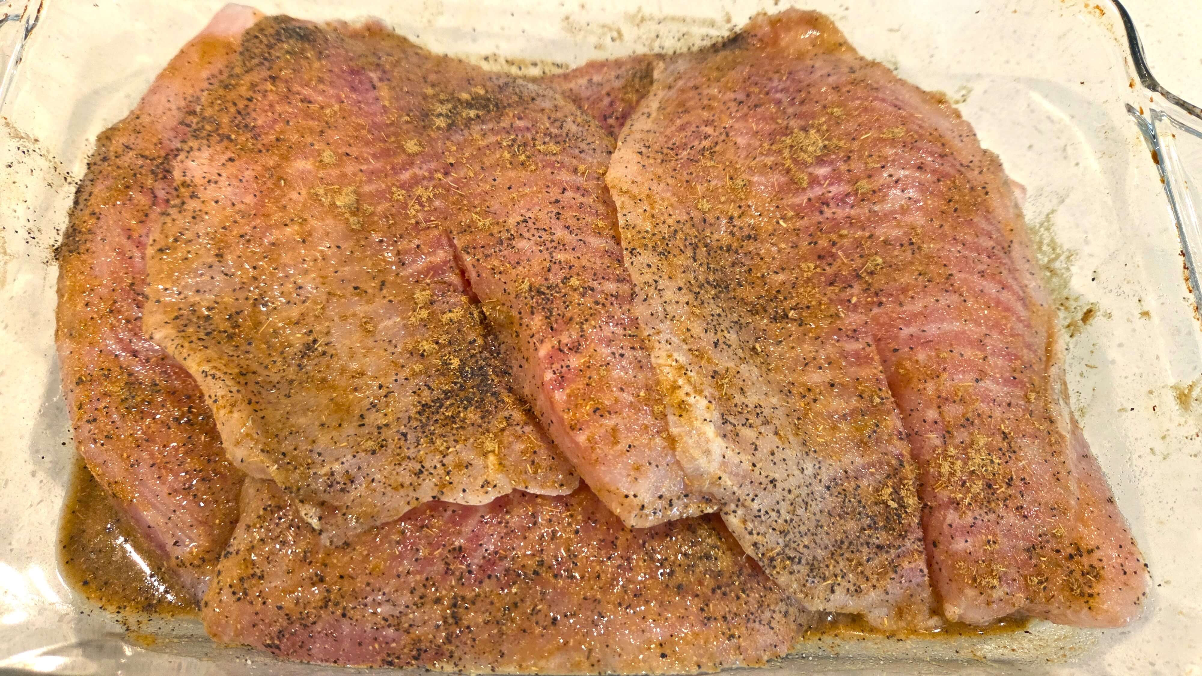 Tilapia fillets seasoned with lemon juice, cumin, coriander, garlic, salt, and black pepper before cooking.