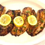 Mediterranean pan seared tilapia in a big serving plate garnishes with chopped parsley and lemon slices.