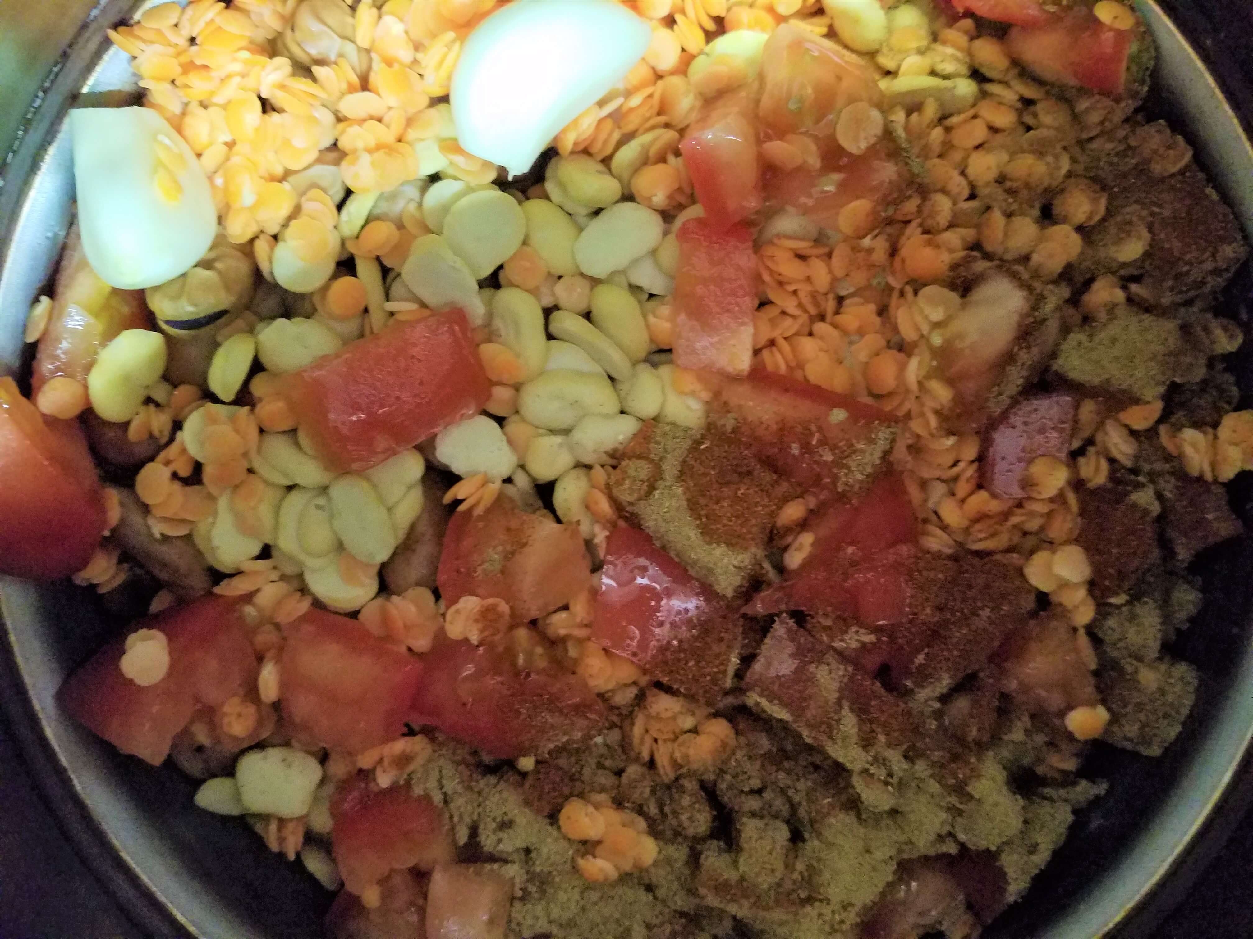 Soaked fava beans combined with split fava beans, red lentils, and garlic cloves in a heavy slow cooker pot.