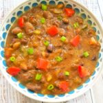 Overhead view of authentic Egyptian Ful Medames in a ceramic bowl drizzled with olive oil, green onion, and diced tomatoes.