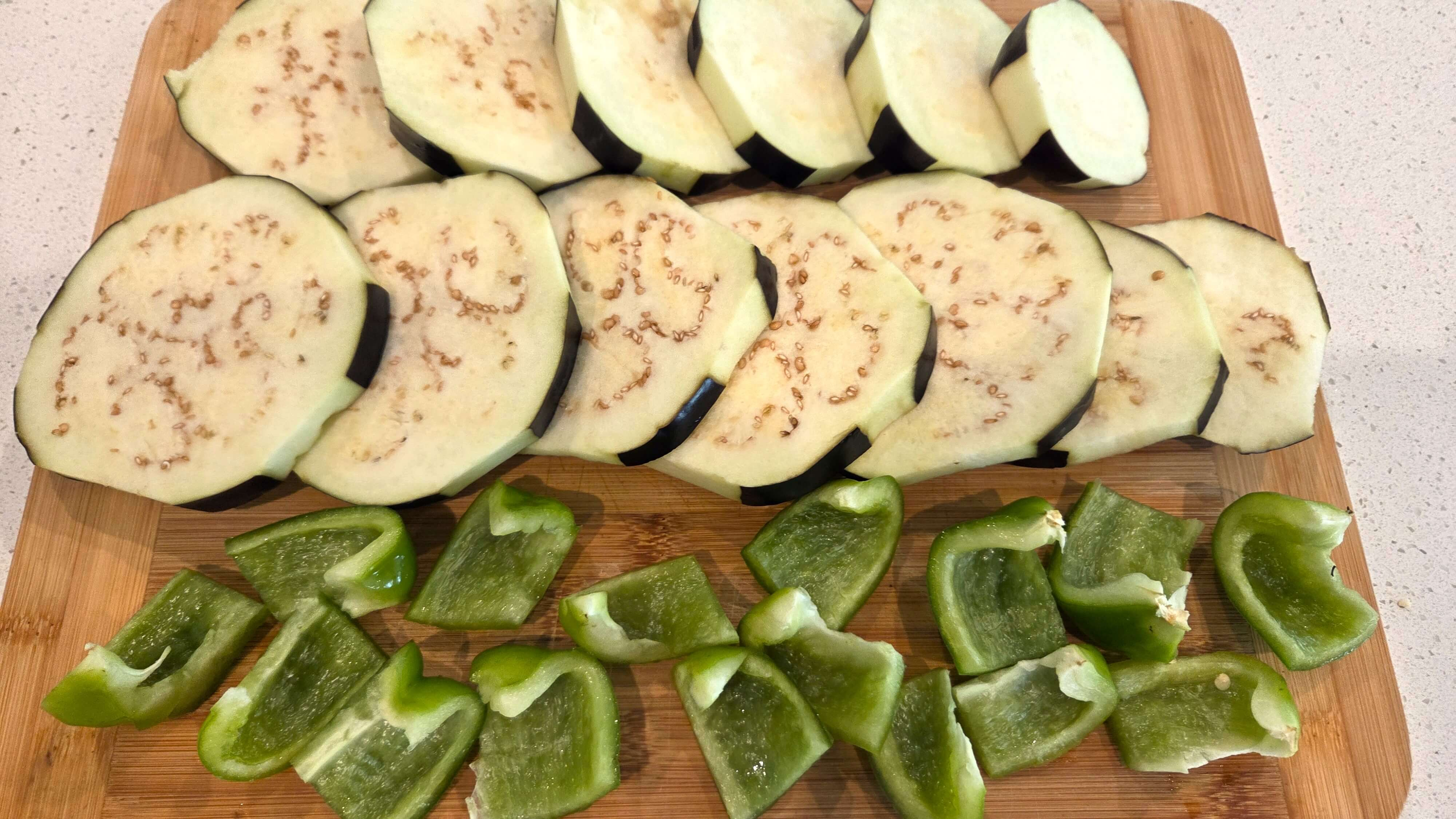 Eggplant peeled in a zebra pattern and green bell pepper cut into large cubes for moussaka.