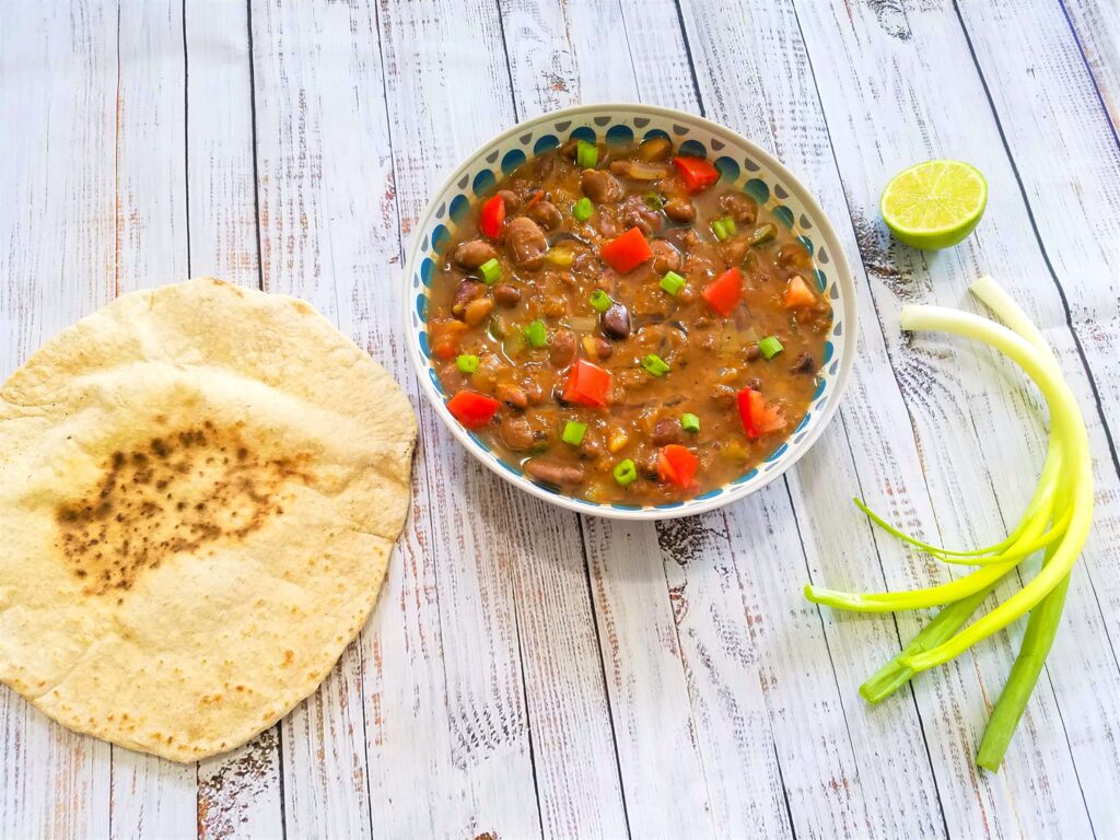 Close-up shot of hot slow-simmered Egyptian Ful Medames in a bowl garnished with fresh chopped tomatoes, green onion, and cumin. Served with pita bread and fresh lime.