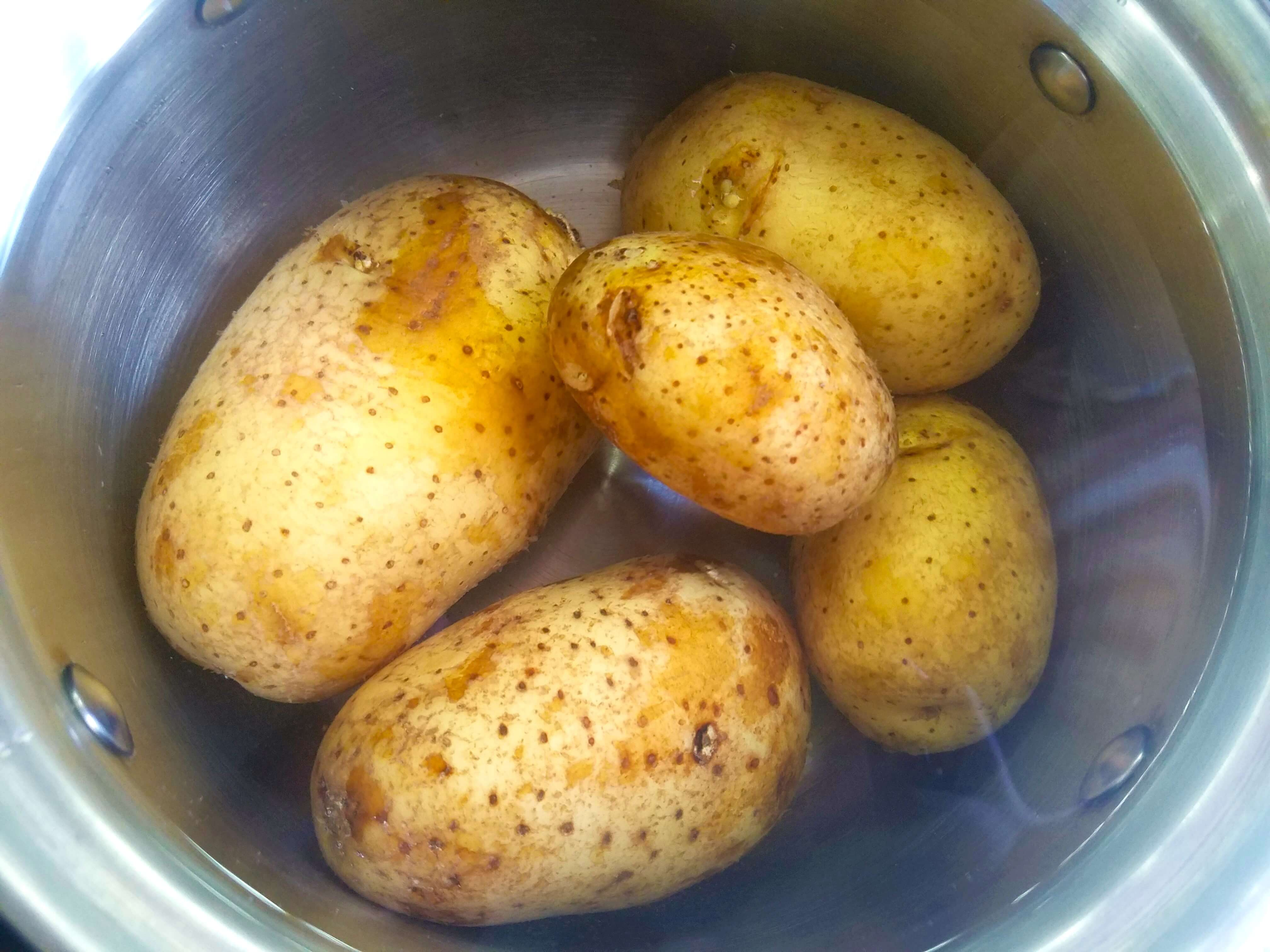 Whole yellow potatoes boiling in a pot for mashed potato salad