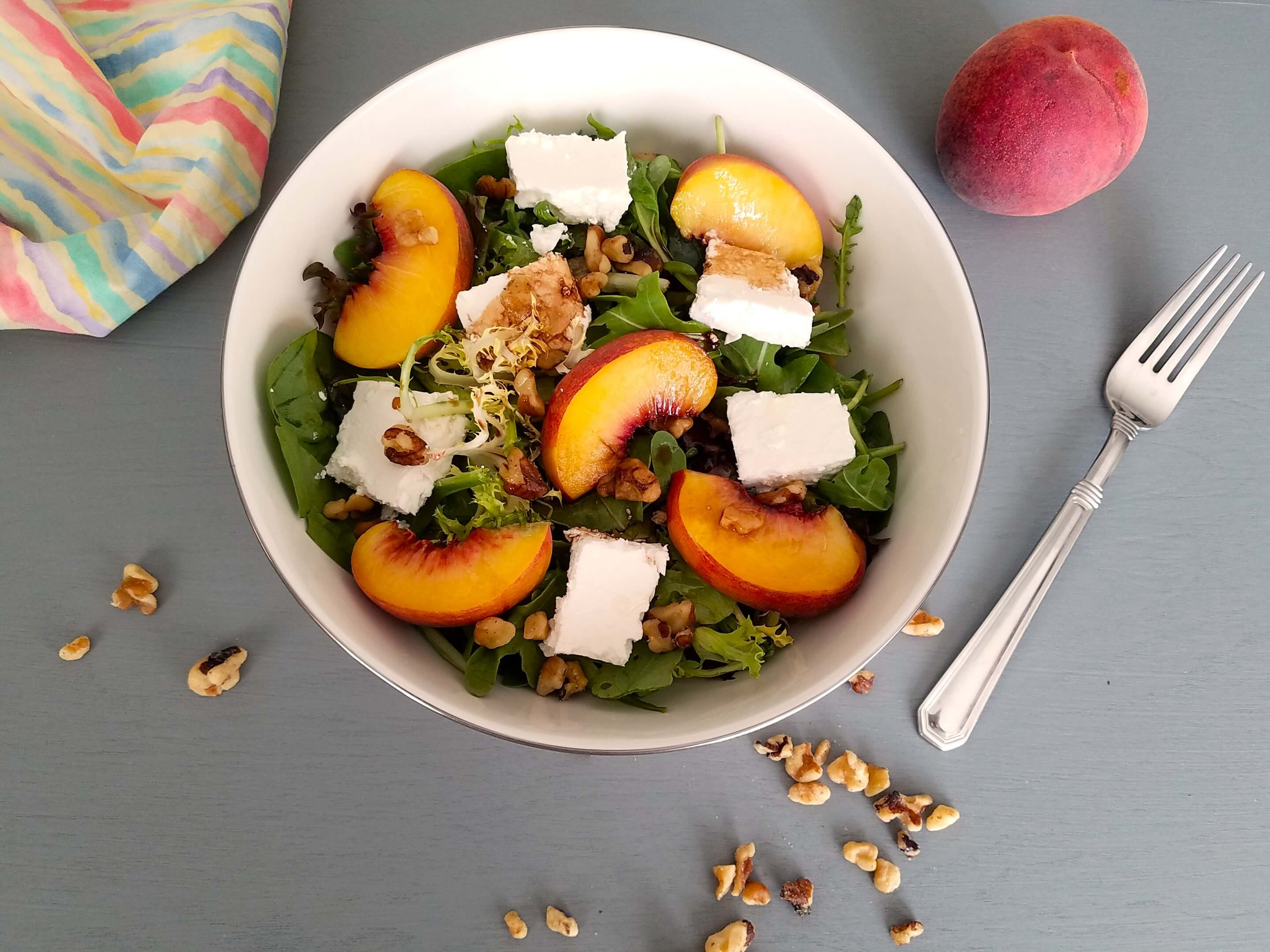 Peach feta salad being tossed with olive oil and balsamic vinegar before serving.