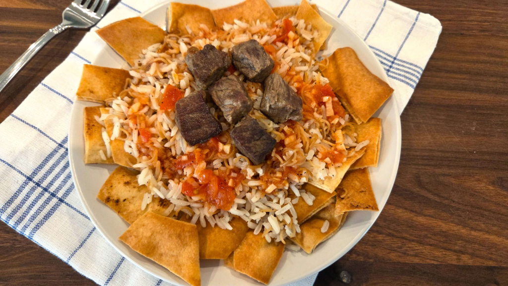 Egyptian Fattah served on a platter with tender beef, fluffy rice, crispy bread, and garlicky tomato sauce.