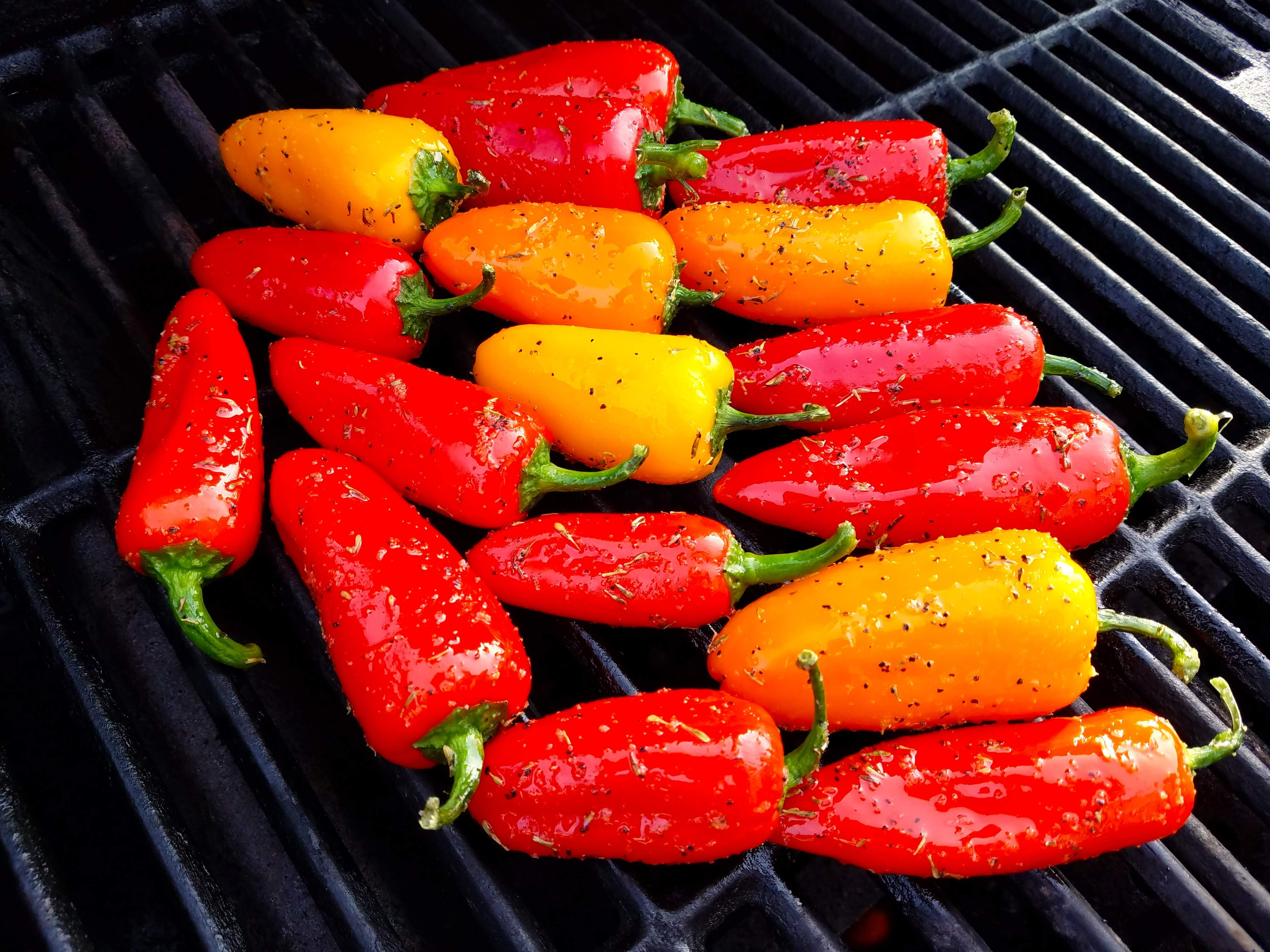 Whole mini peppers grilling on a hot outdoor grill
