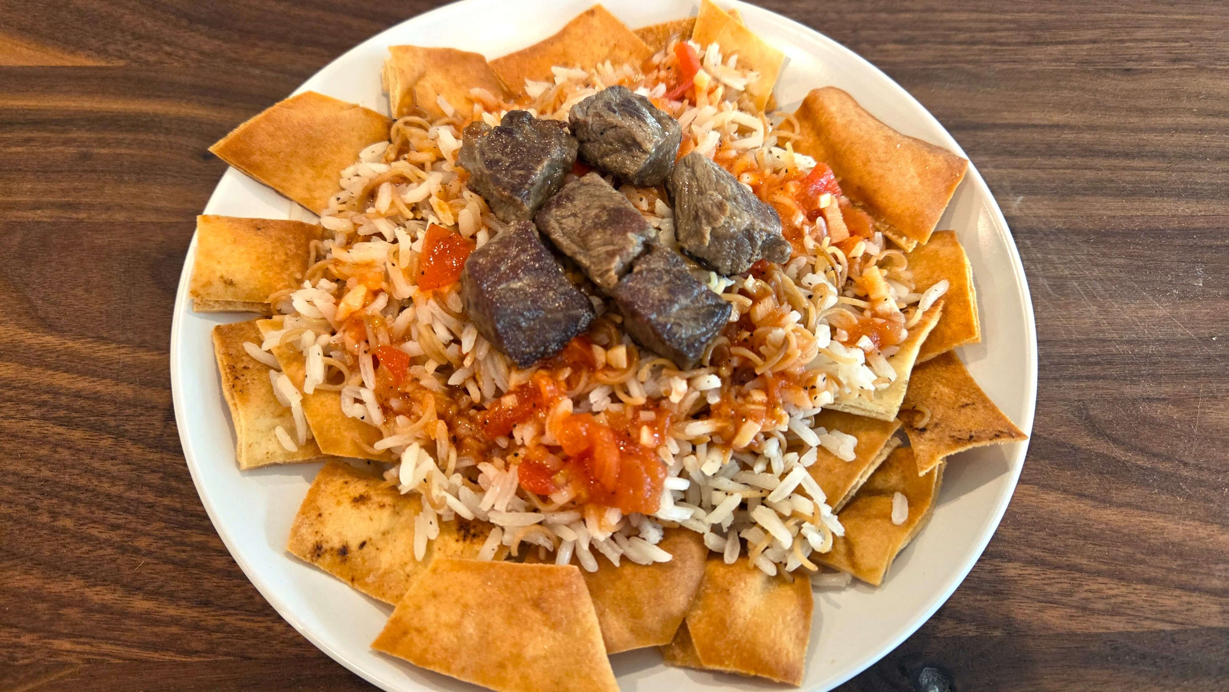 Crispy bread, vermicelli rice, browned beef, and garlic-vinegar tomato sauce layered to make Egyptian Fattah.