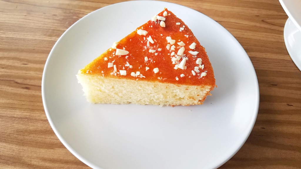 Slice of Moroccan apricot cake with apricot jam and almonds served on white ceramic plate.