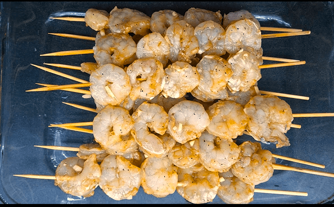 Marinated shrimp threaded onto wooden skewers before grilling.
