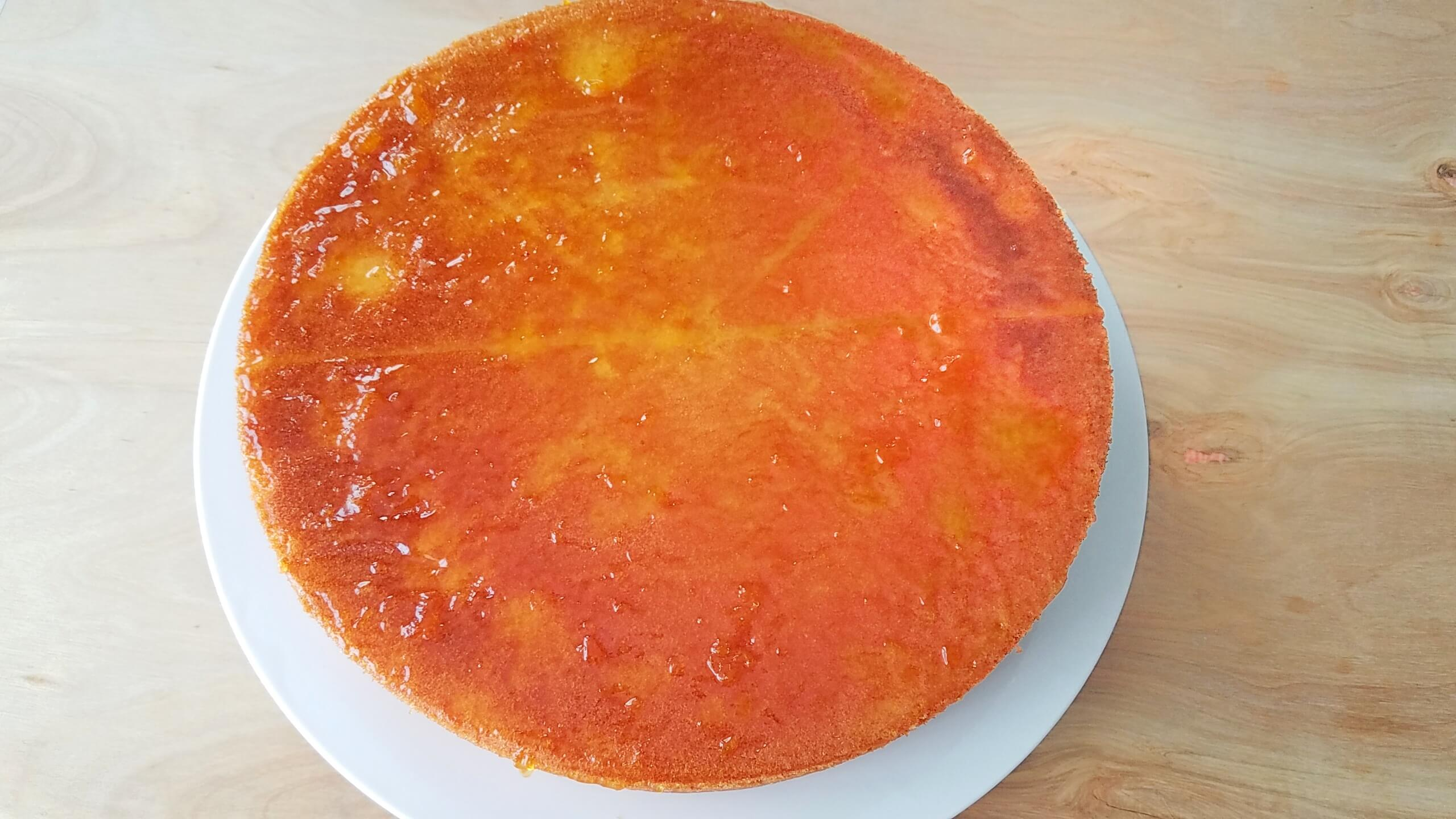 Apricot jam being spread over the top of the cooled cake.
