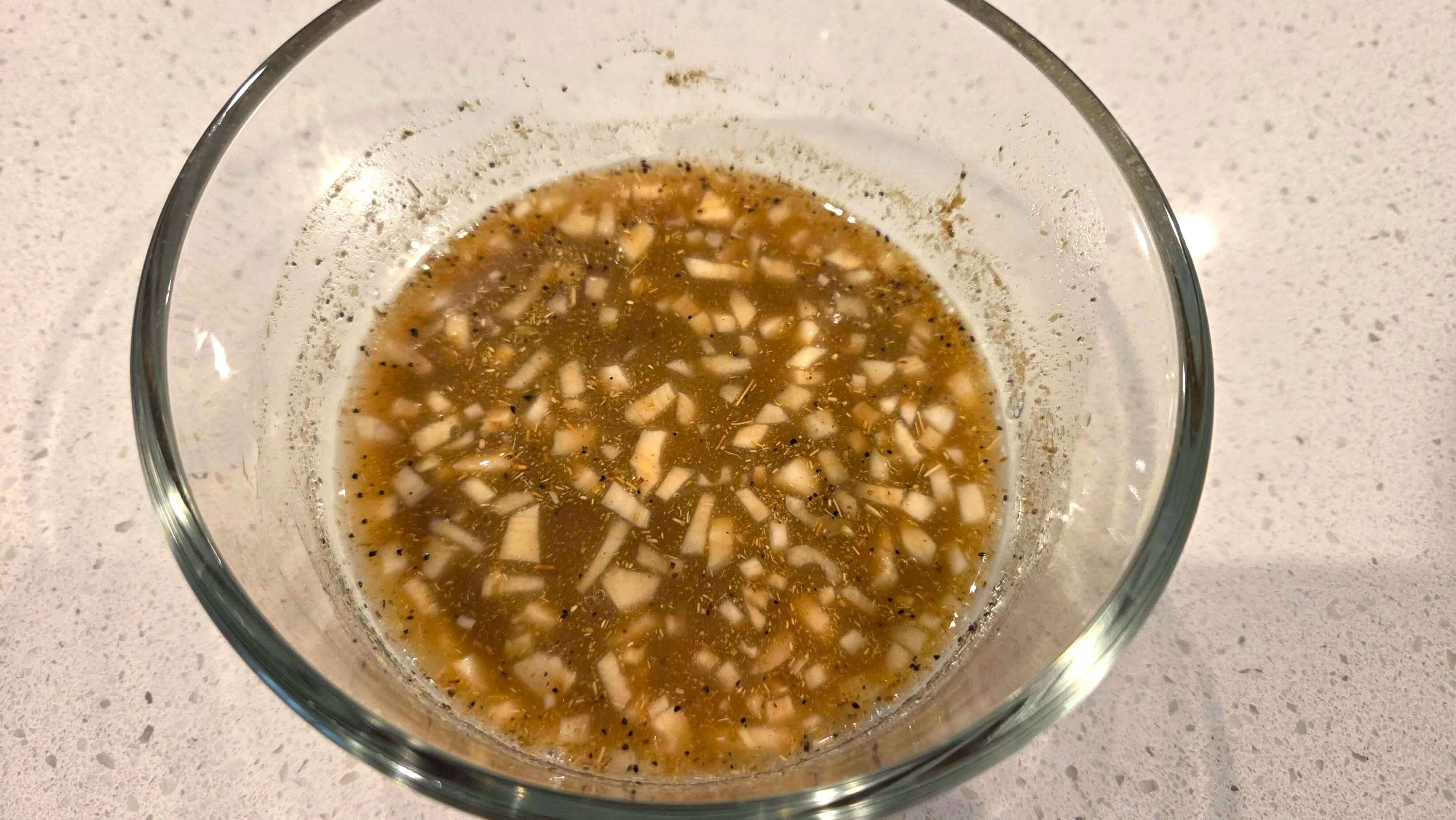 Minced garlic, lemon juice, white vinegar, cumin, coriander, salt, and black pepper mixed for eggplant salad dressing.