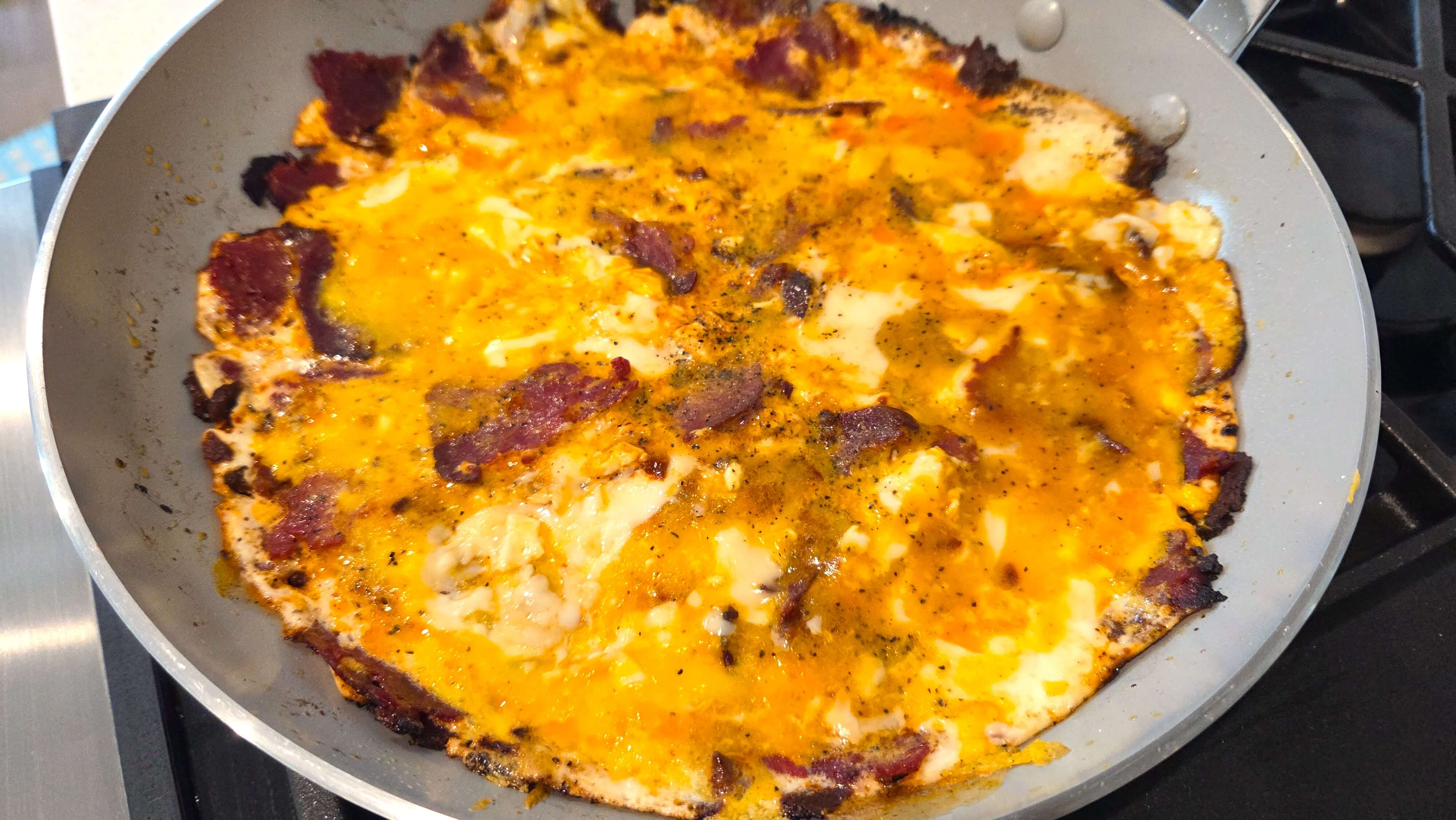 Soft scrambled eggs being folded with basturma in a skillet
