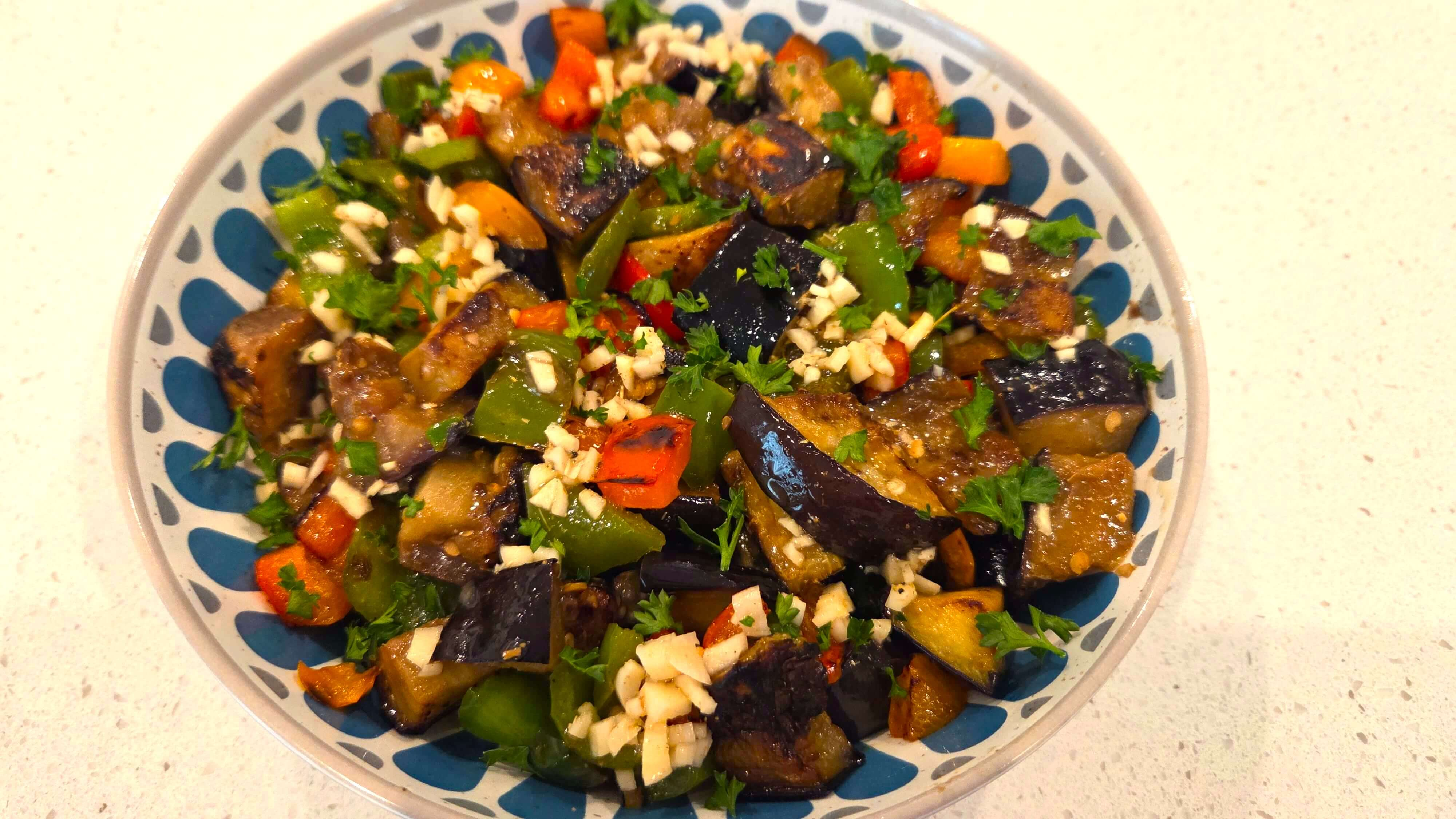Fried eggplant and sautéed bell peppers tossed with chopped parsley and tangy garlic dressing in a bowl.